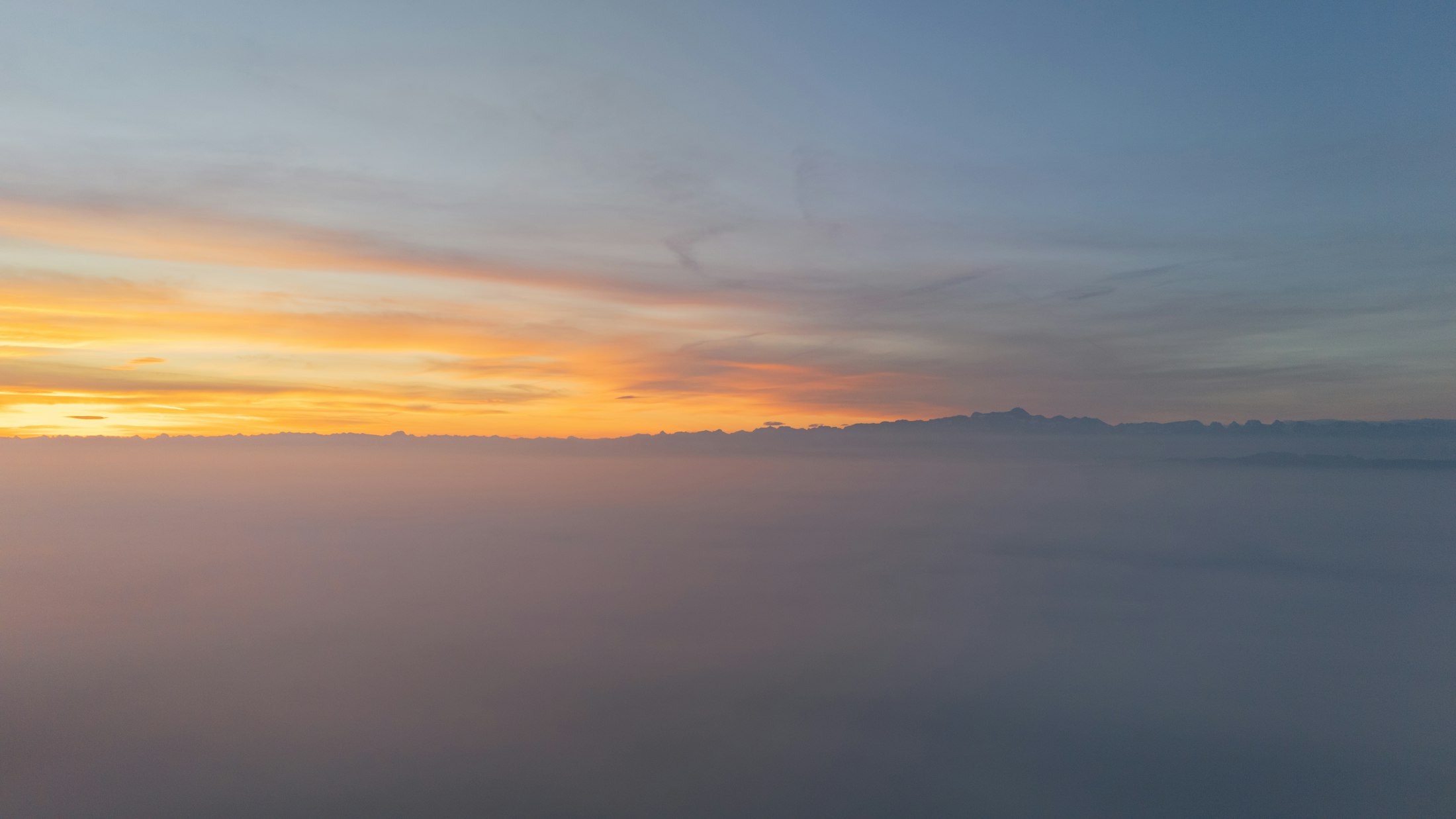 Mar de neblina fria sobre um vale da Serra Catarinense ao amanhecer, com a silhueta das montanhas no horizonte.