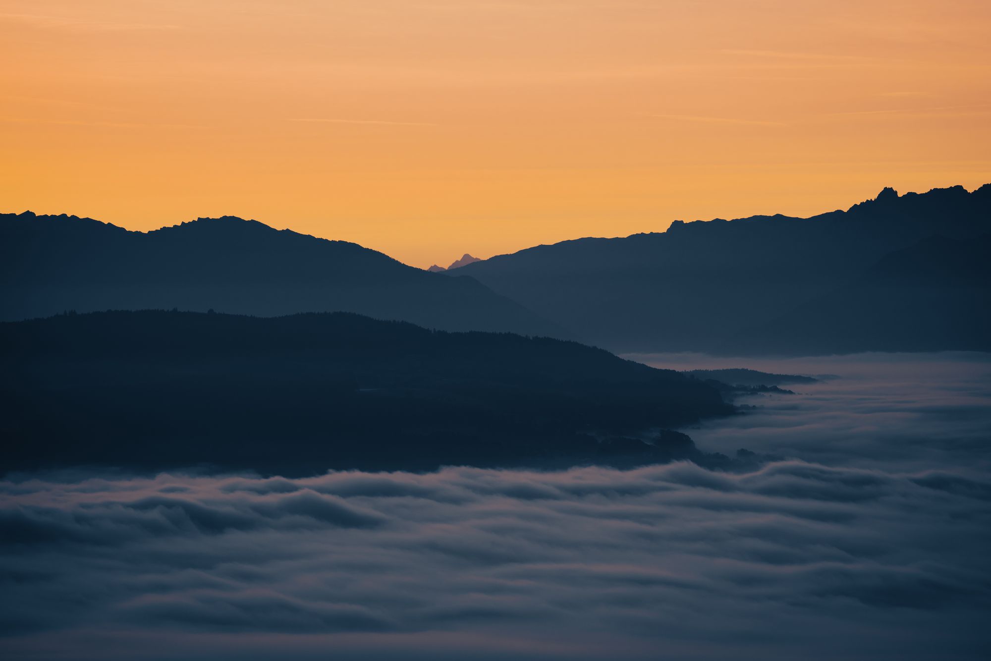 Camadas de cristas de serra com neblina no vale e céu âmbar de amanhecer.